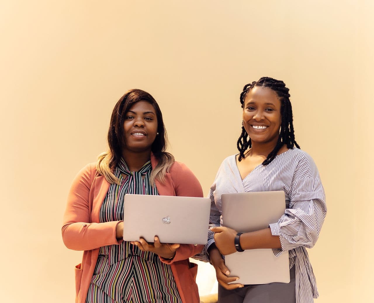 Two women entrepreneurs smiling and holding laptops, for Women & Wealth Kenya